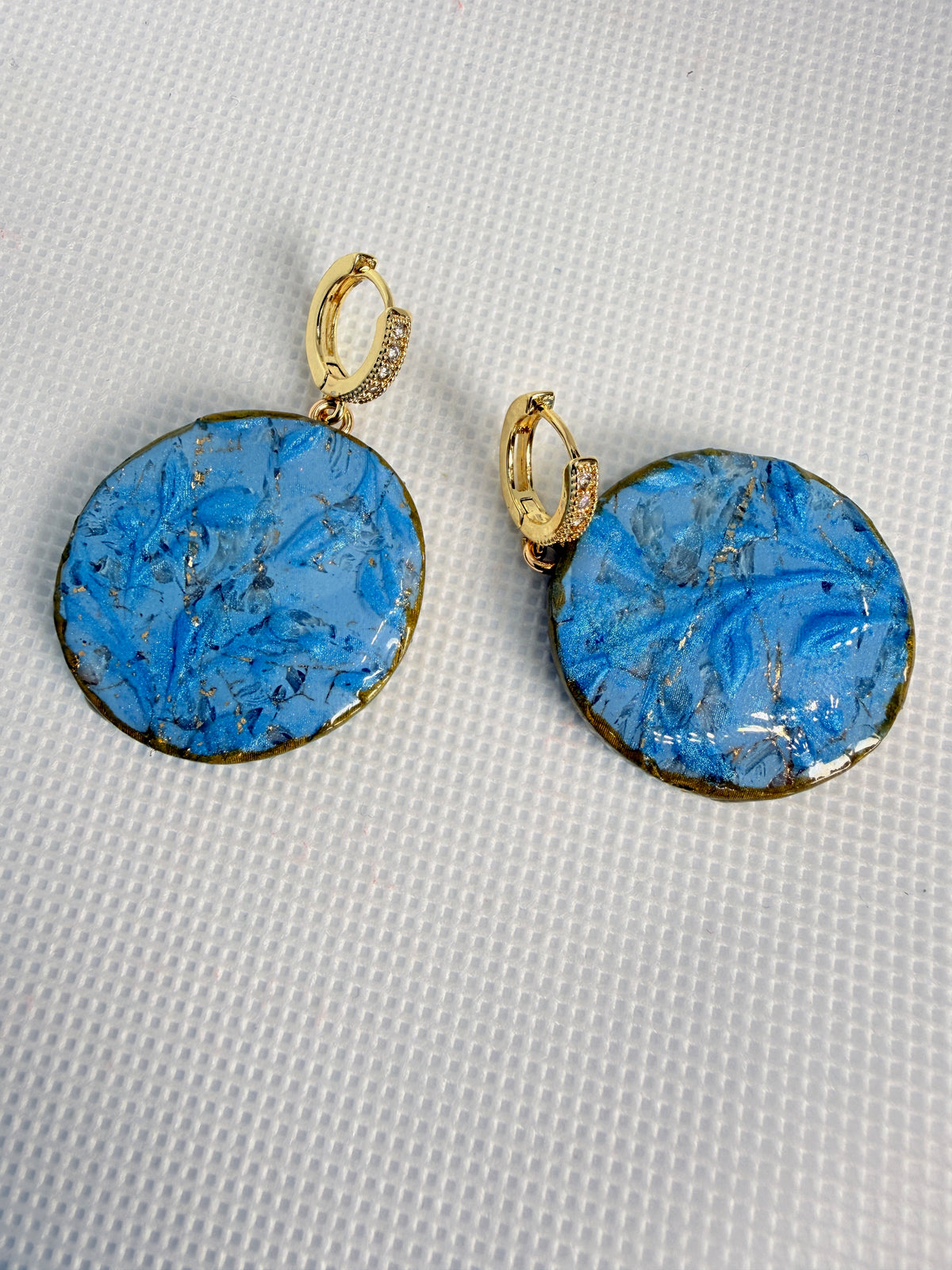 Flora Blue handmade polymer clay earrings, blue discs with raised floral texture and gold edges on crystal-set gold hoops
