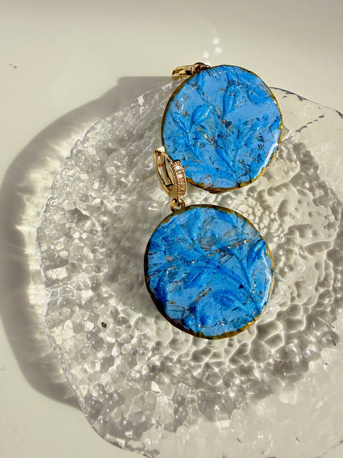 Flora Blue polymer clay statement earrings styled on a textured glass dish in sunlight