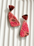 Rosa Coral polymer clay statement earrings with carved pink roses and gold-tone rings, styled on a white ribbed tray
